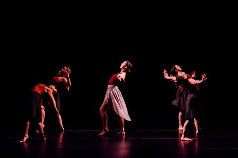 Four lyrical dancers around a central dancer. The dancers are wearing maroon leotards and lavender, calf-length skirts. The dancers are lit with side light and appear as though they are in a black void.