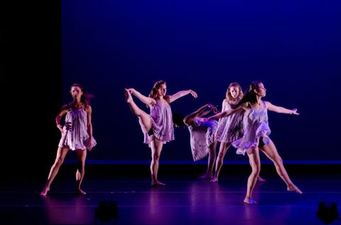Five dancers in various poses are wearing lavender, flowing, lyrical dresses. They are lit with cool side light and lavender back light. You can see faint reflections of the dancers in the marley floor.