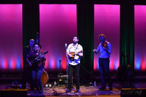 The band Steel Wheels stand on a rug. There is a magenta cyc and columns created by black legs in the background. The band is lit by blue back light and wrm white back specials. The singer in the middle is in a warm front special.