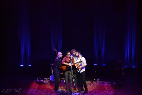 The band Steel Wheels group around a center vocal microphone. There are uplit columns in the background.