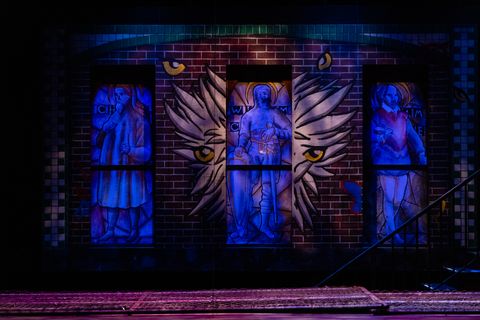 Brick wall with three stained glass windows with human figures painted in black light paint.